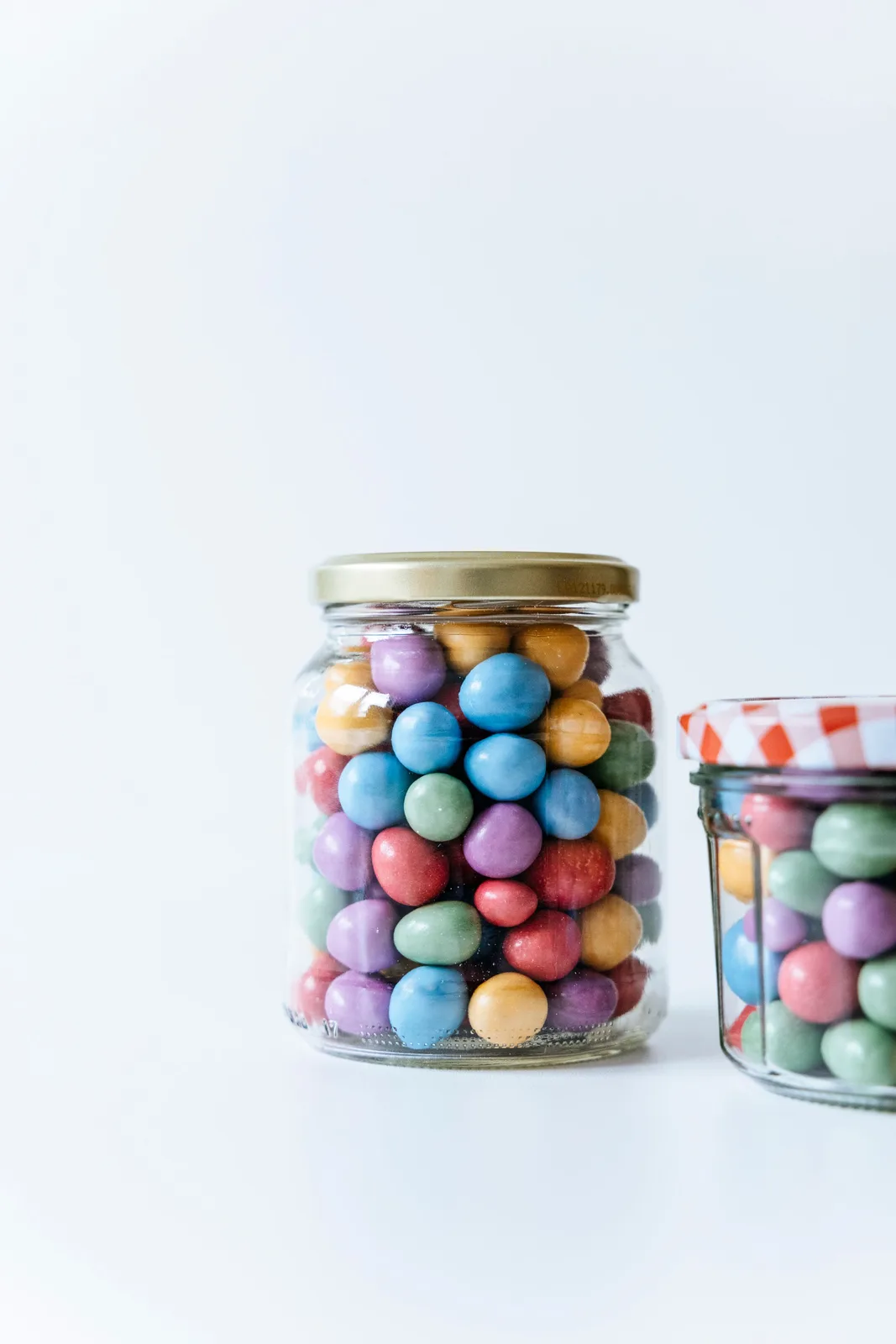 Colorful candies in two glass jars, one under a red-checked lid