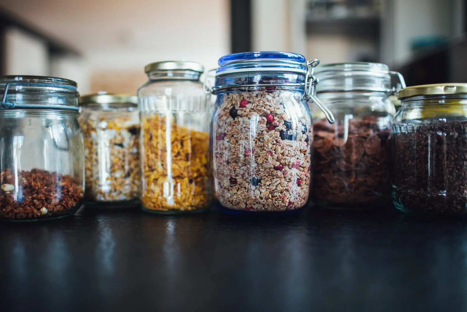 Glass jars of granola and cereal in a row on a dark counter